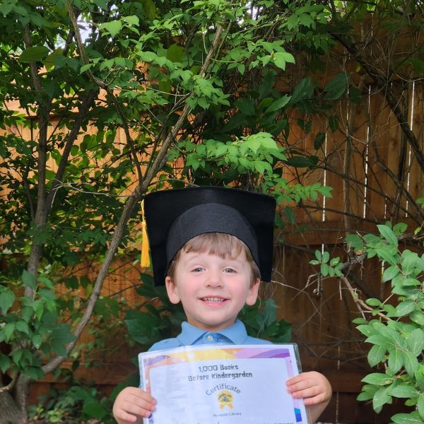 A recent 1000 Books graduate, James, wearing a graduation cap and holding his graduation certificate.